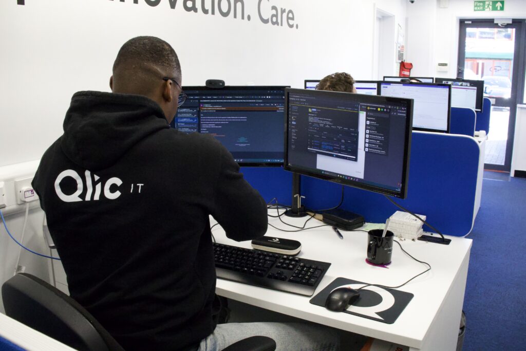 A Qlic IT technician for nonprofits working at a dual-monitor workstation as IT support